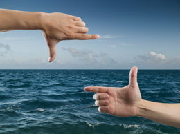 Hands creating a frame for an ocean and sky scene