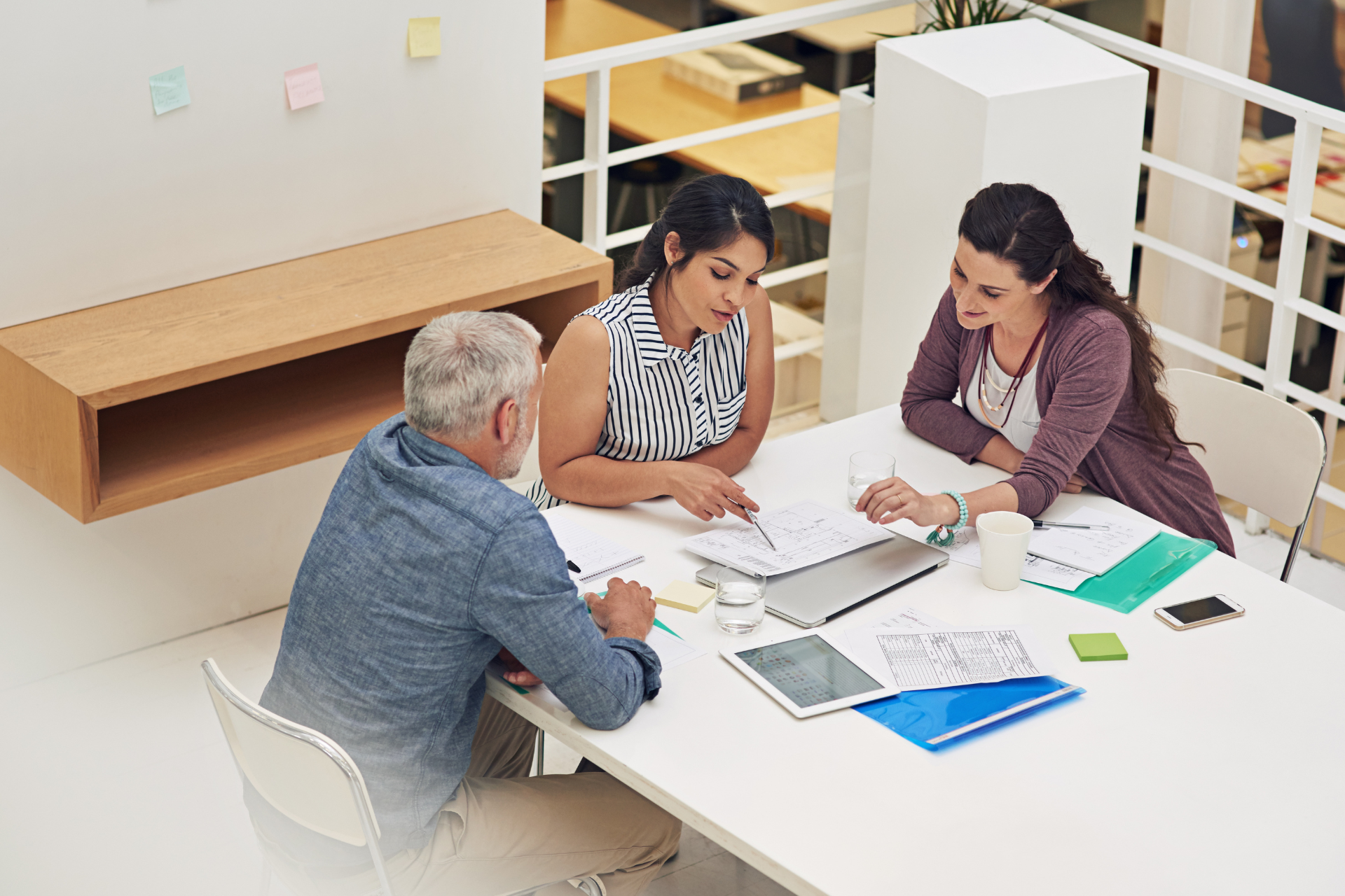 3 people sit at a table in a library looking at research documents