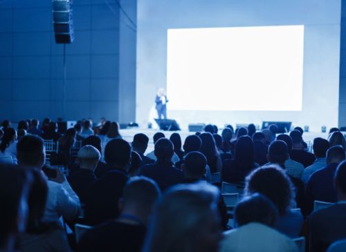A far-away look at a person giving a presentation in front of a large screen