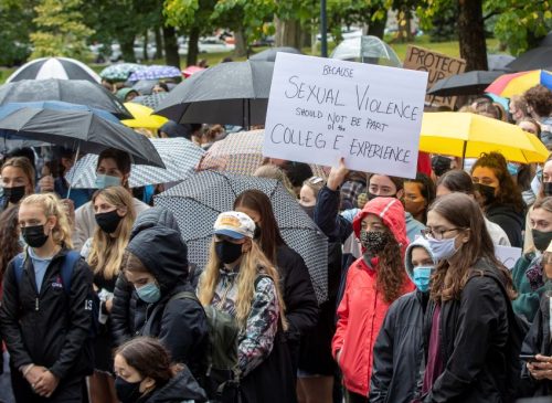 A group of masked protesters in the rain outside holding signs,