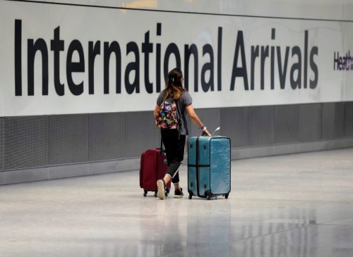 A person wheels two suitcases by a large sign that says International Arrivals.